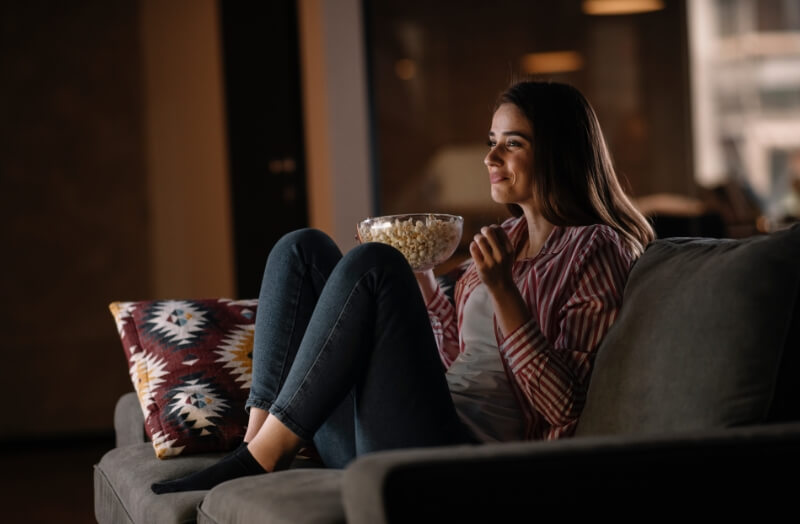 A woman is watching a movie on tv with a bowl of popcorn